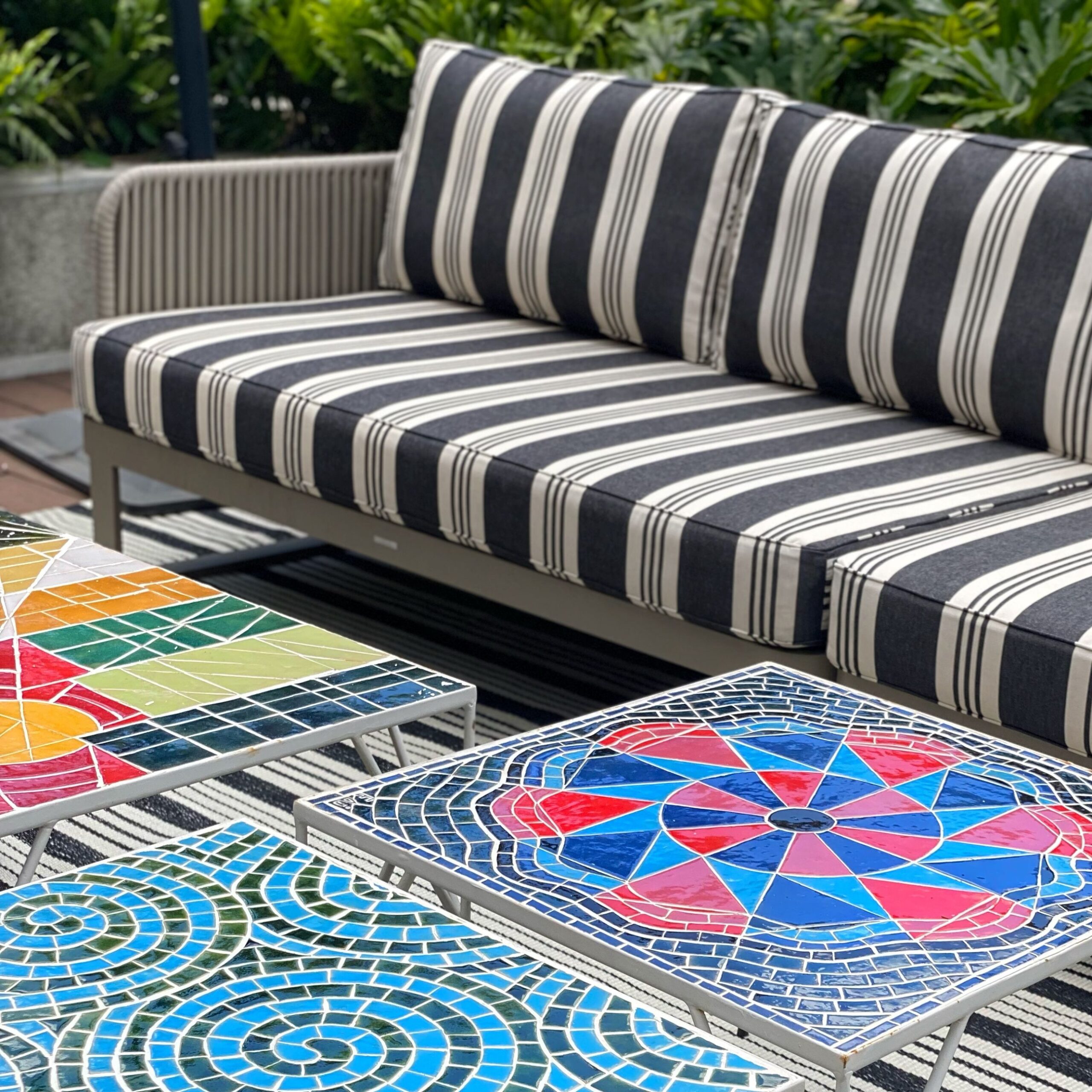 tres mesas decoradas con mosaicos y mueble de terraza con tela de rayas