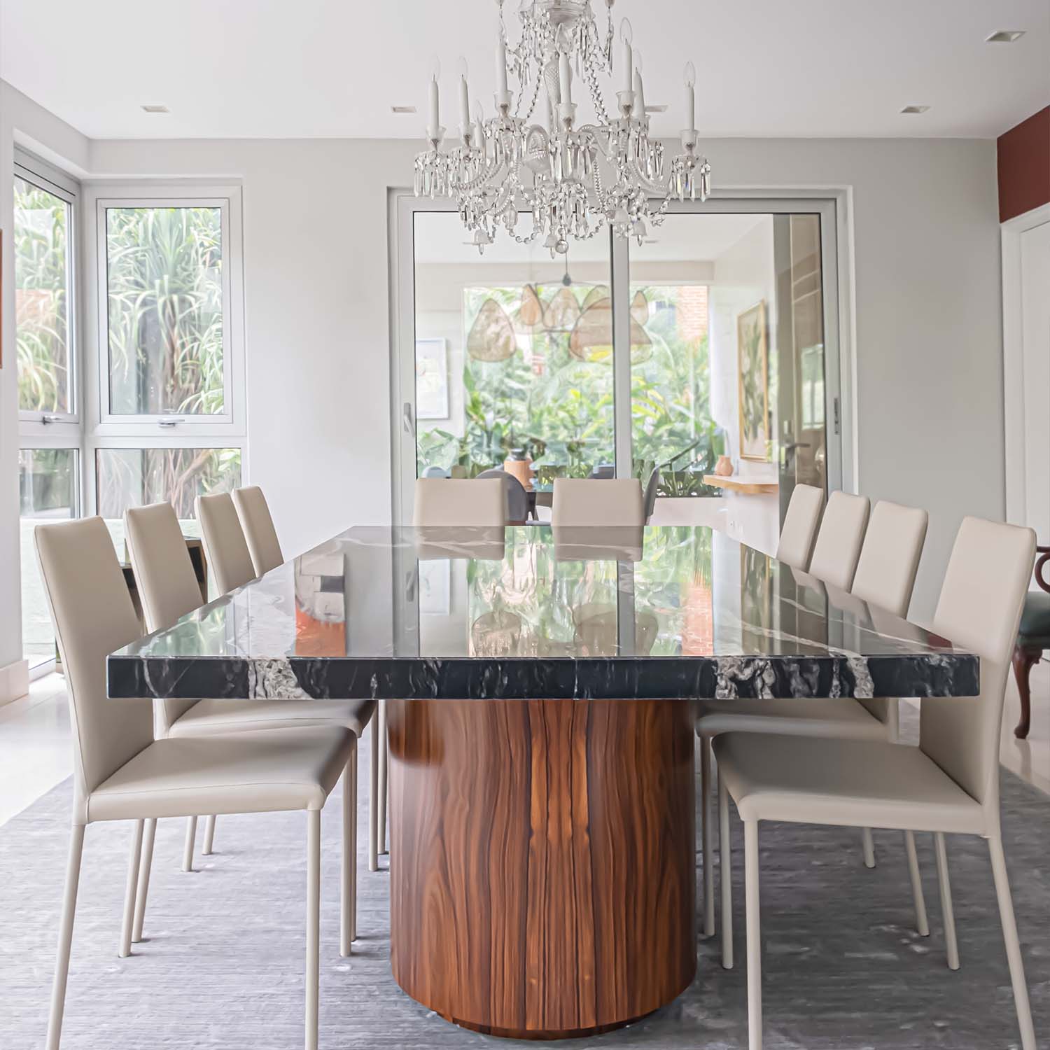 A contemporary dining space with a wooden table, a striking black granite countertop, white chairs, and a stylish chandelier.