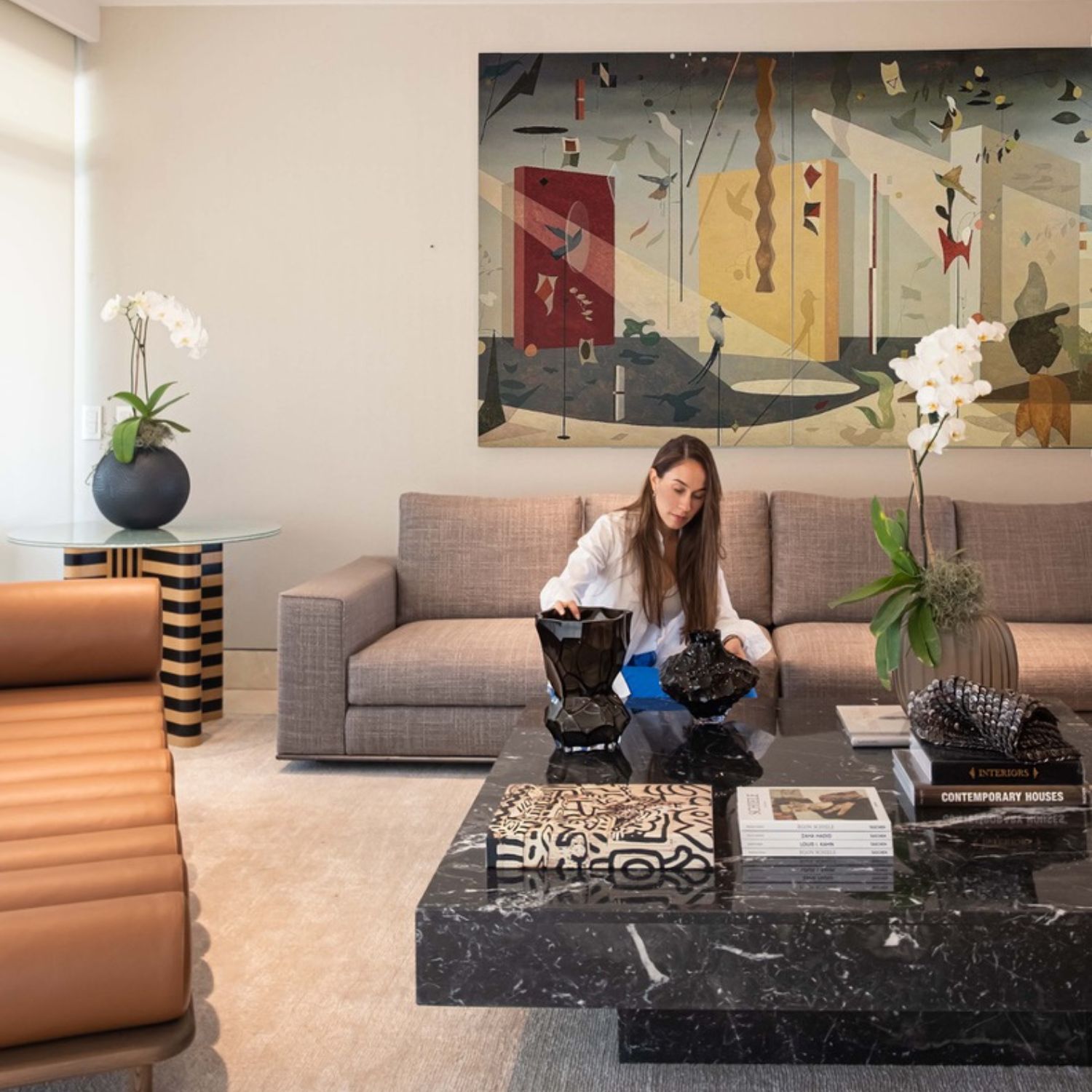 Designer Ana Volante styling the black marble coffee table with sculptural vases and design books, beneath a contemporary art painting.