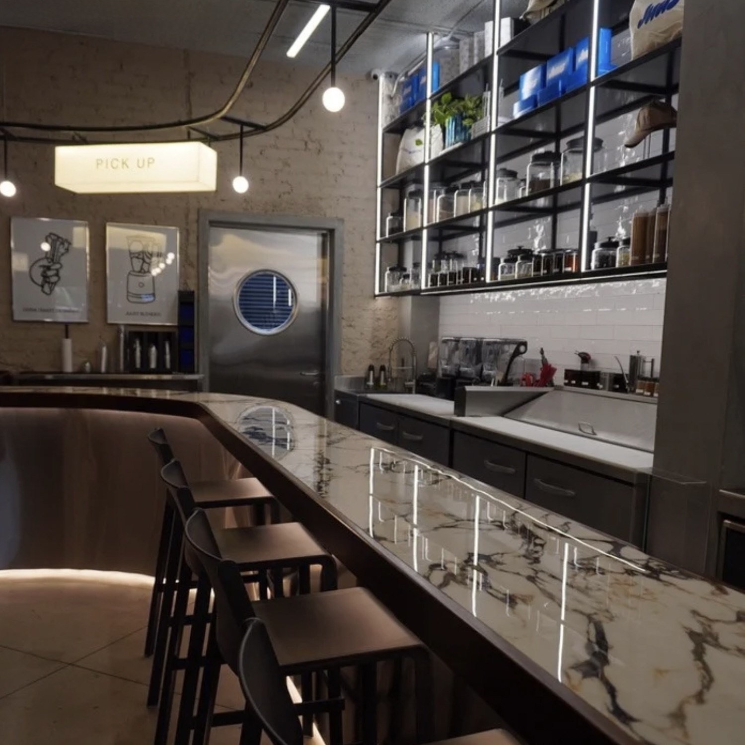 Coffe bar at SWIITCH Gym Caracas with marble countertop, high chairs and modern shelving.