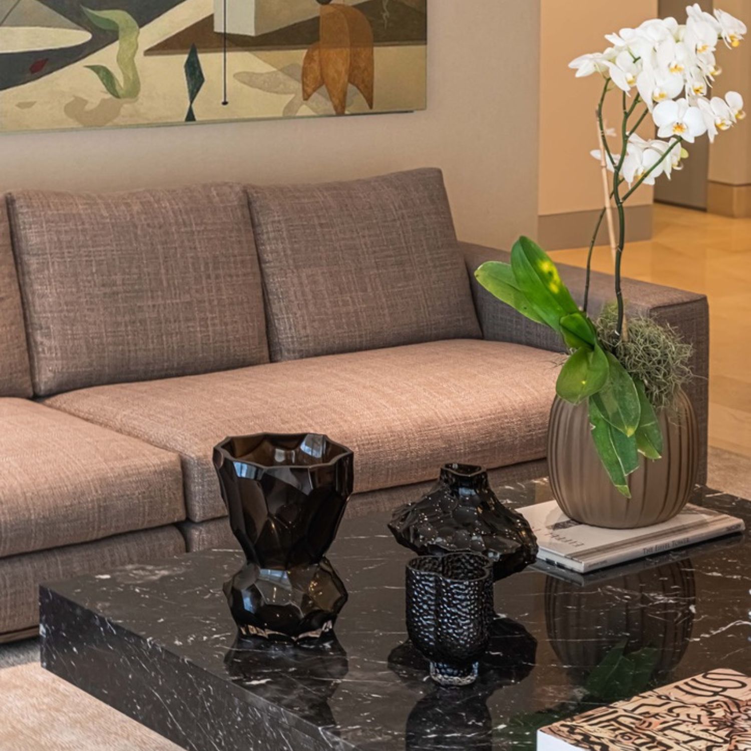 Close-up of gray sofa next to black marble coffee table decorated with black vases and white orchid in a beige vase.