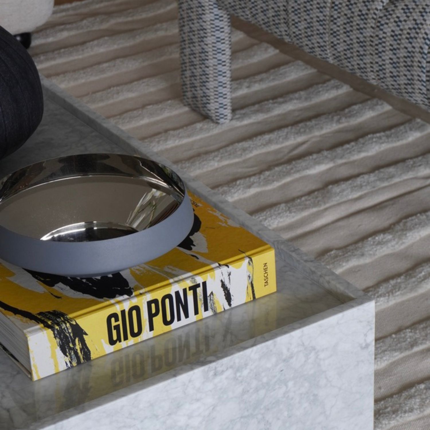 Detalle de mesa de centro de mármol con libro de diseño Gio Ponti y bandeja metálica decorativa.
