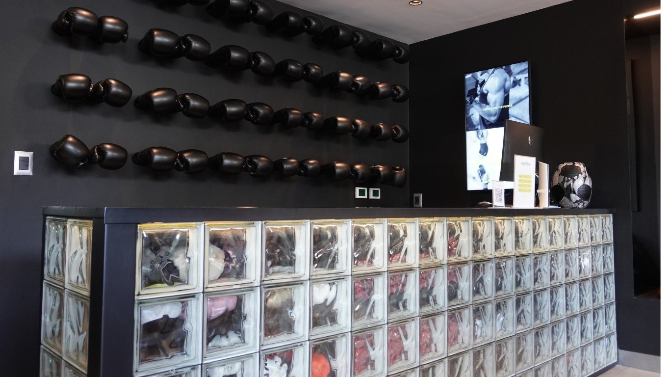 Recepción del gimnasio SWIITCH en Caracas con mostrador de bloques de vidrio y pared decorada con guantes de boxeo negros.