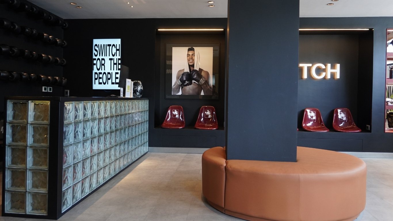 Recepción del gimnasio SWIITCH Caracas con mostrador de bloques de vidrio, sillas modernas y un gran retrato de boxeador.