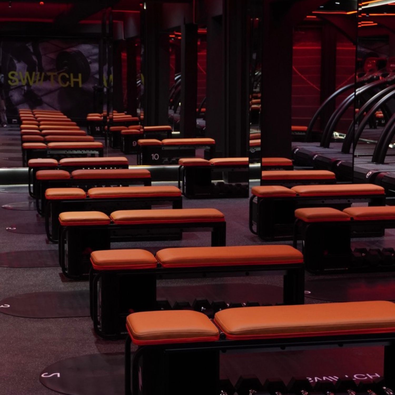 Sala de entrenamiento del gimnasio SWIITCH en Caracas, con estaciones numeradas, iluminación LED roja y espejos que amplifican el espacio.