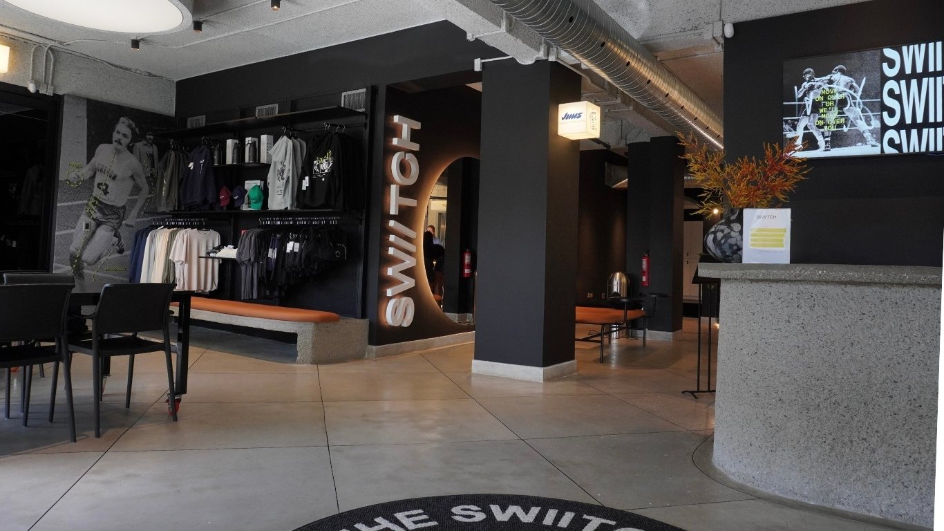 Vista general del lobby del gimnasio SWIITCH Caracas, con murales deportivos, iluminación cálida y mobiliario minimalista.