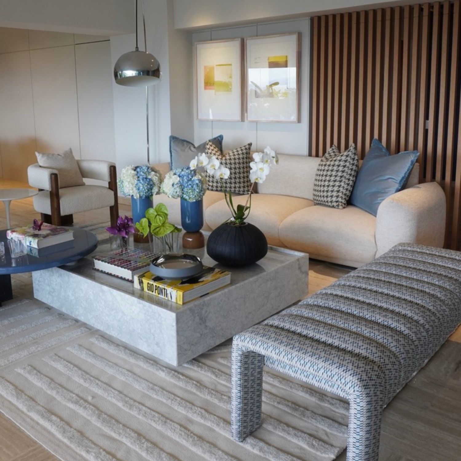 Sala contemporánea con sofá beige, cojines en tonos azul y blanco y negro, mesa de centro de mármol y flores decorativas, Proyecto Residencial 22.