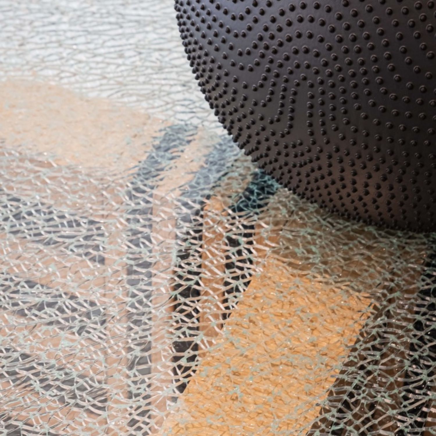 Primer plano de Cross Round Table by Ana Volante: mesa de vidrio texturizado con base en tonos cálidos y jarrón decorativo en cerámica oscura