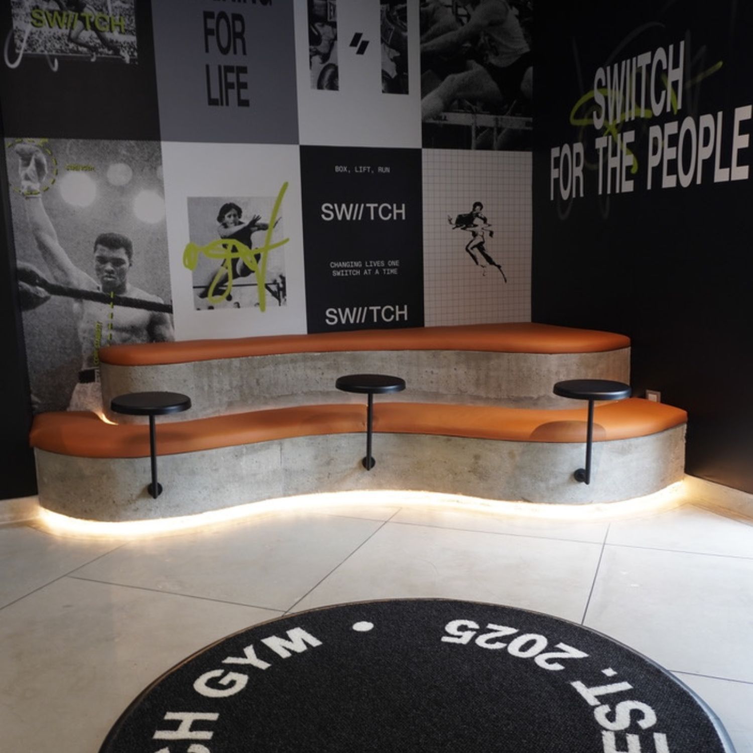 Área de espera con bancos tapizados en cuero naranja para el proyecto de diseño interior del gimnasio SWIITCH Altamira por Ana Volante.