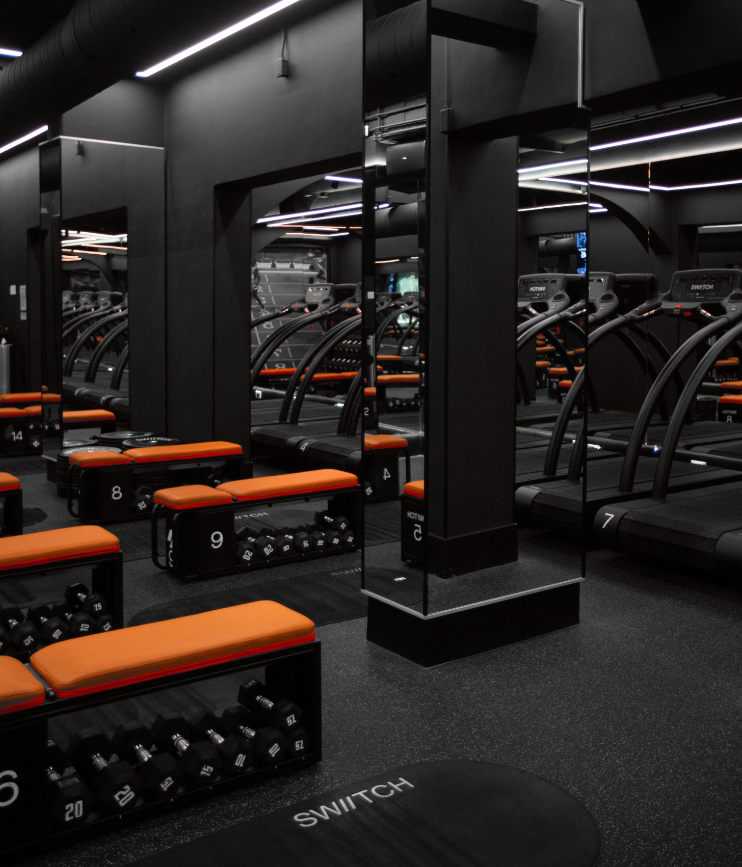 Functional training room at Swiitch Gym Caracas with curved treadmills, mirrors, strength benches, and modern black interior design