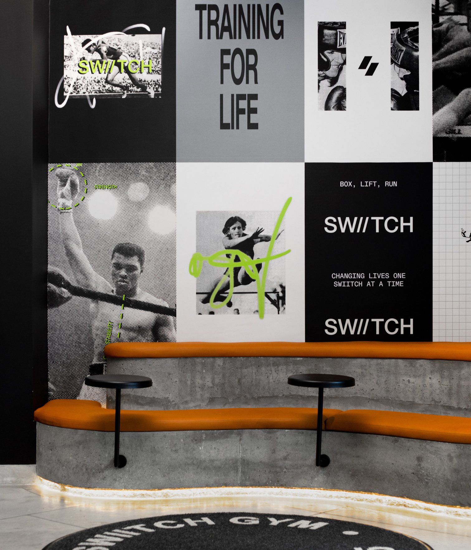 Waiting area at Swiitch Gym Caracas with concrete seating, orange cushions, and graphic wall murals with boxing-inspired visuals