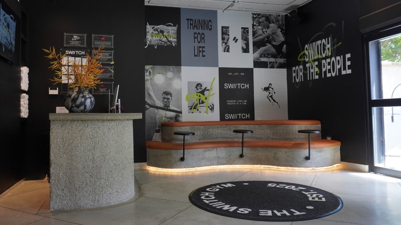 Área de espera del gimnasio SWIITCH en Altamira Caracas, con murales deportivos y bancas de concreto con asientos de cuero.