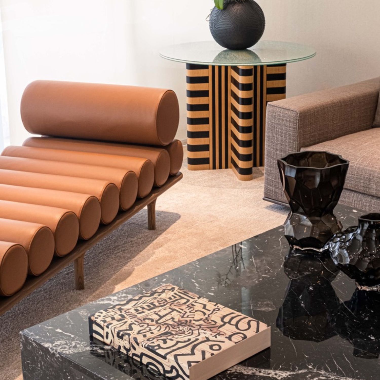 Detail of terracotta leather chaise lounge next to round side table with geometric black and gold base.