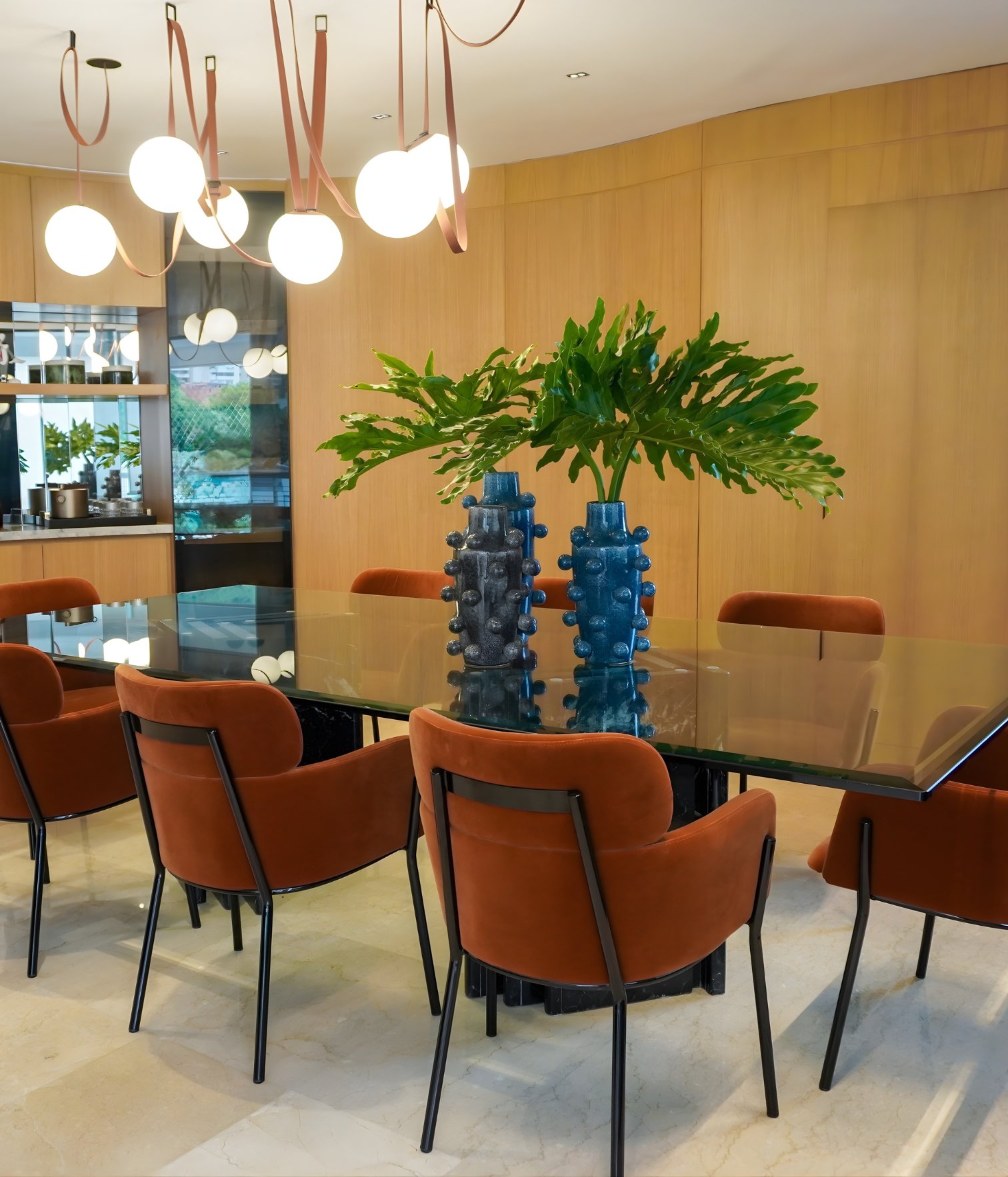 Elegant dining room with glass table, upholstered chairs and sculptural pendant lighting designed by Ana Volante.