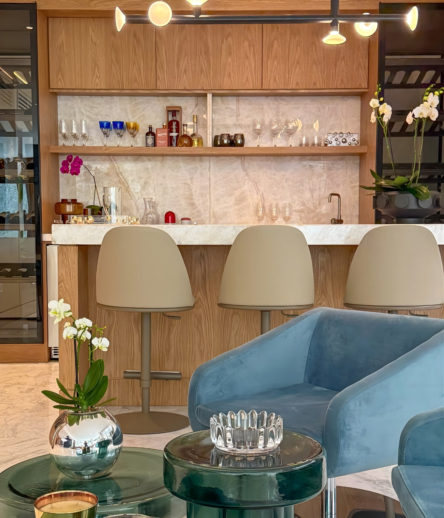 Vista frontal del bar integrado con taburetes, estanterías de madera y fondo de mármol iluminado en proyecto residencial de Volante Studio