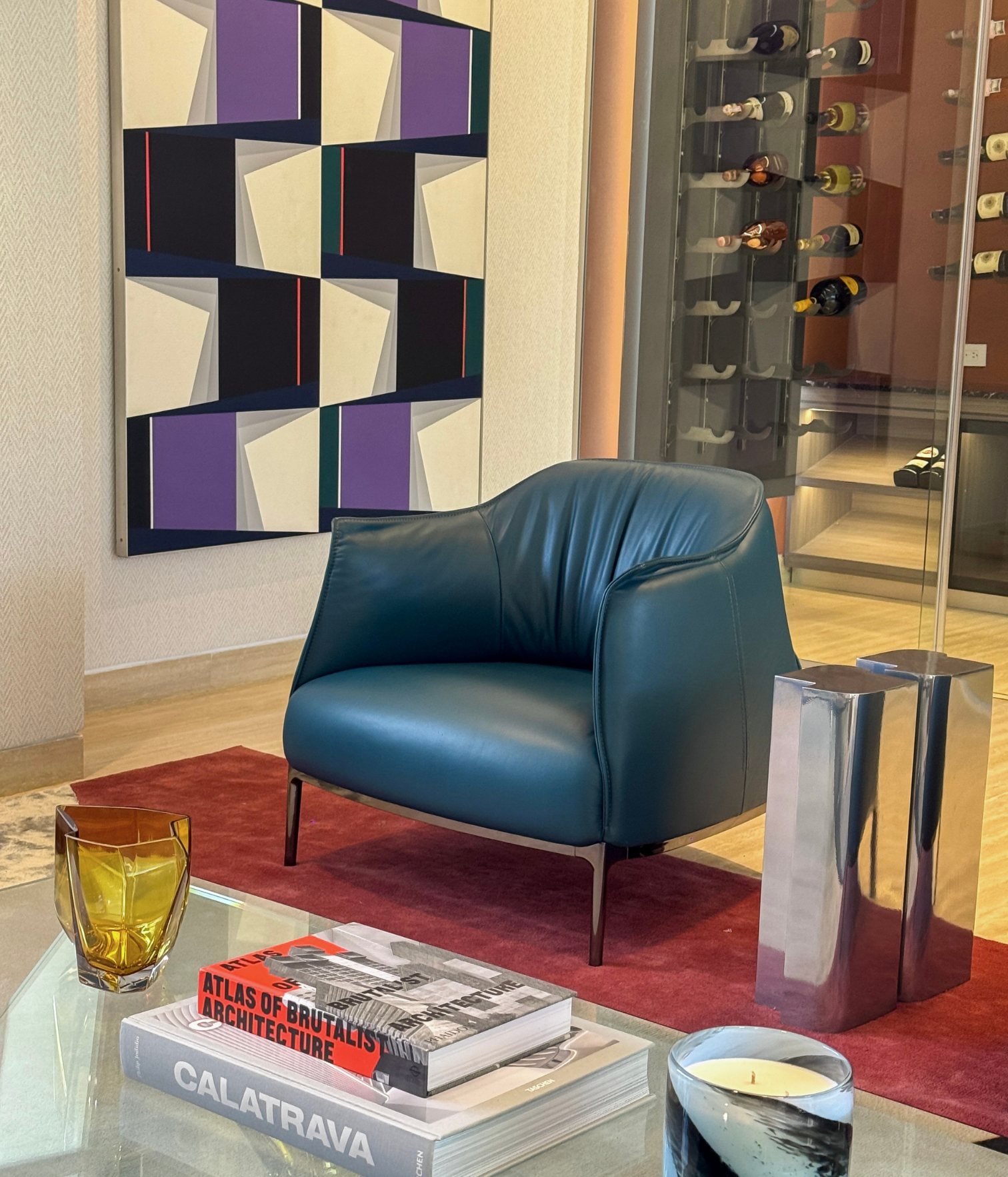 Butaca de cuero azul oscuro sobre alfombra roja con obra de arte geométrica y cava de vinos al fondo