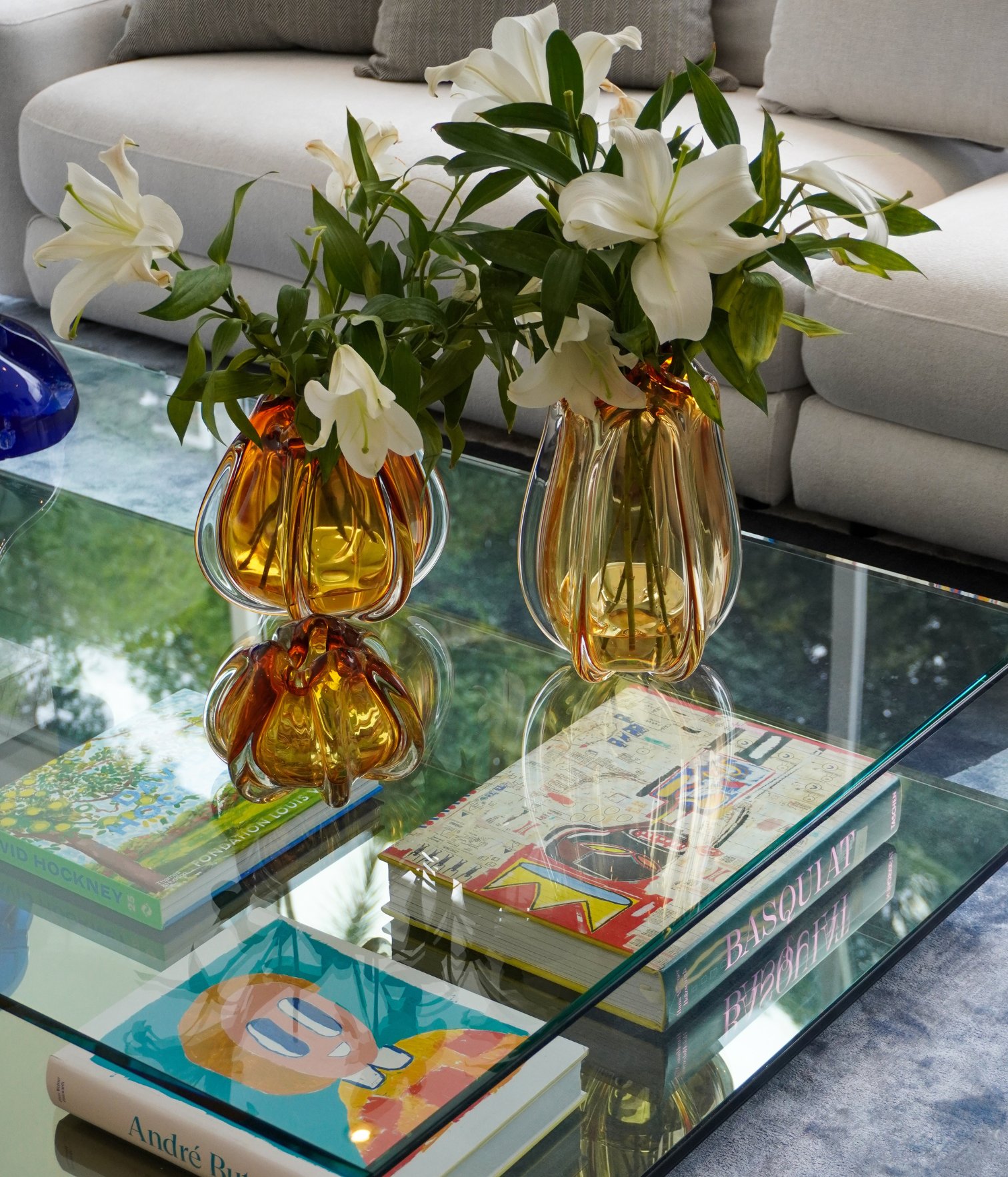 Detail of amber glass vases with white lilies on glass coffee table with art books