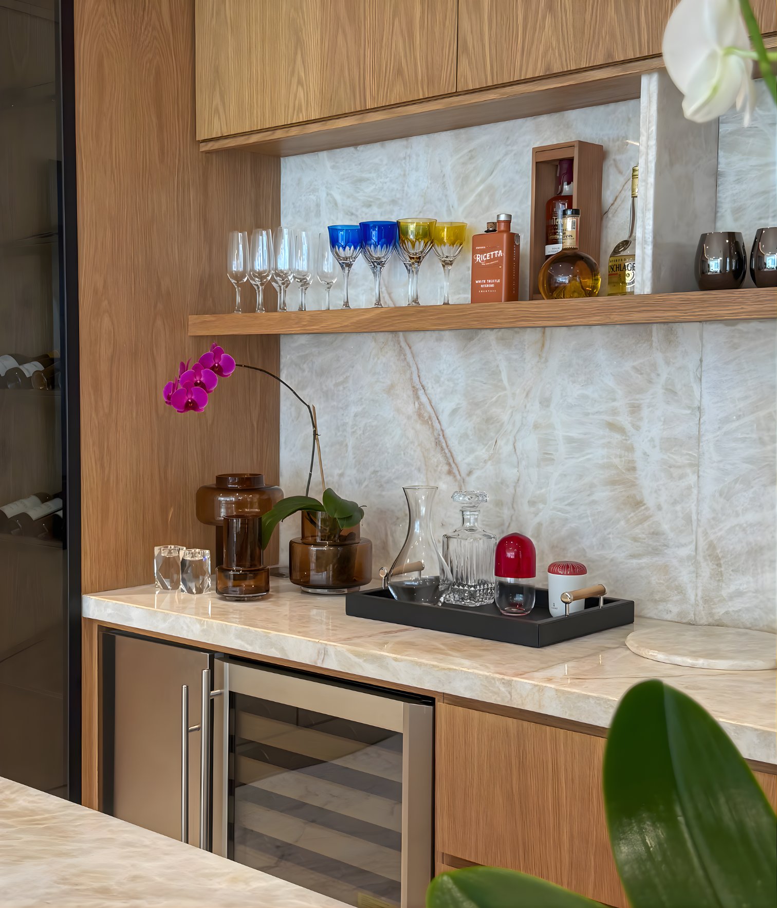 Detalle del bar residencial con encimera de mármol, cristalería, botellas y decoración con orquídea