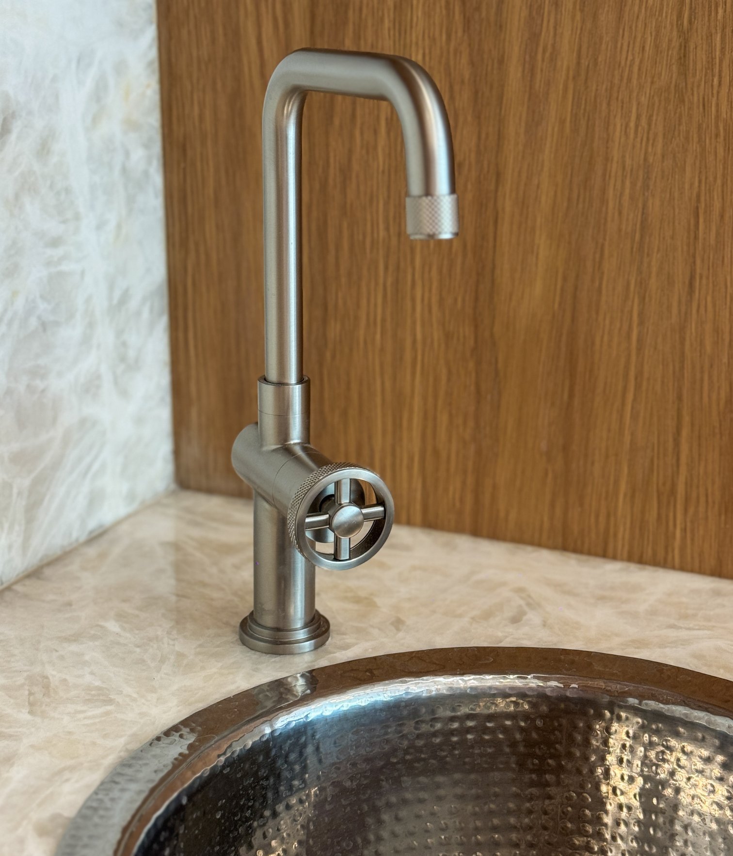 Grifo metálico de diseño contemporáneo sobre encimera de mármol junto a fregadero texturizado en bar residencial