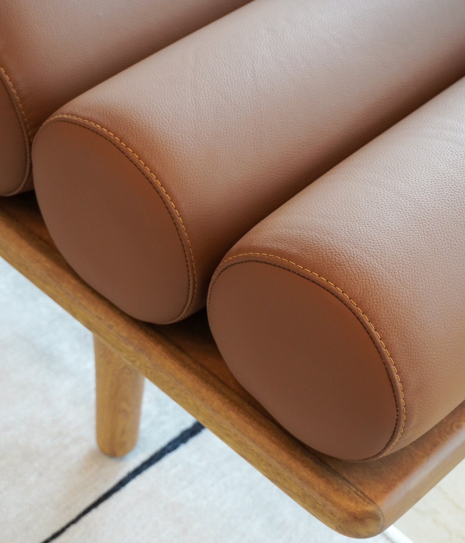 Close-up detail of a leather upholstered bench with wooden base in a contemporary living room interior by Ana Volante.