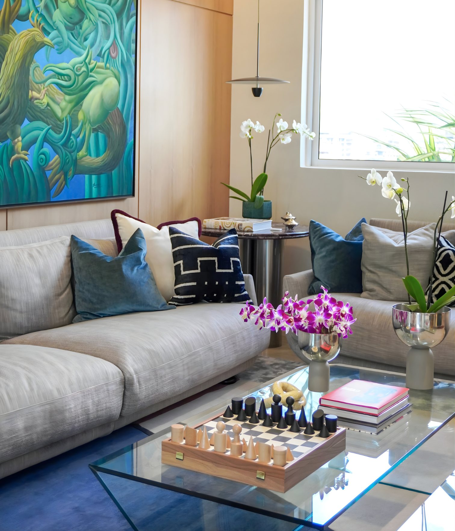 Contemporary living room with gray sofa, blue cushions and large green-toned artwork on wood-paneled wall