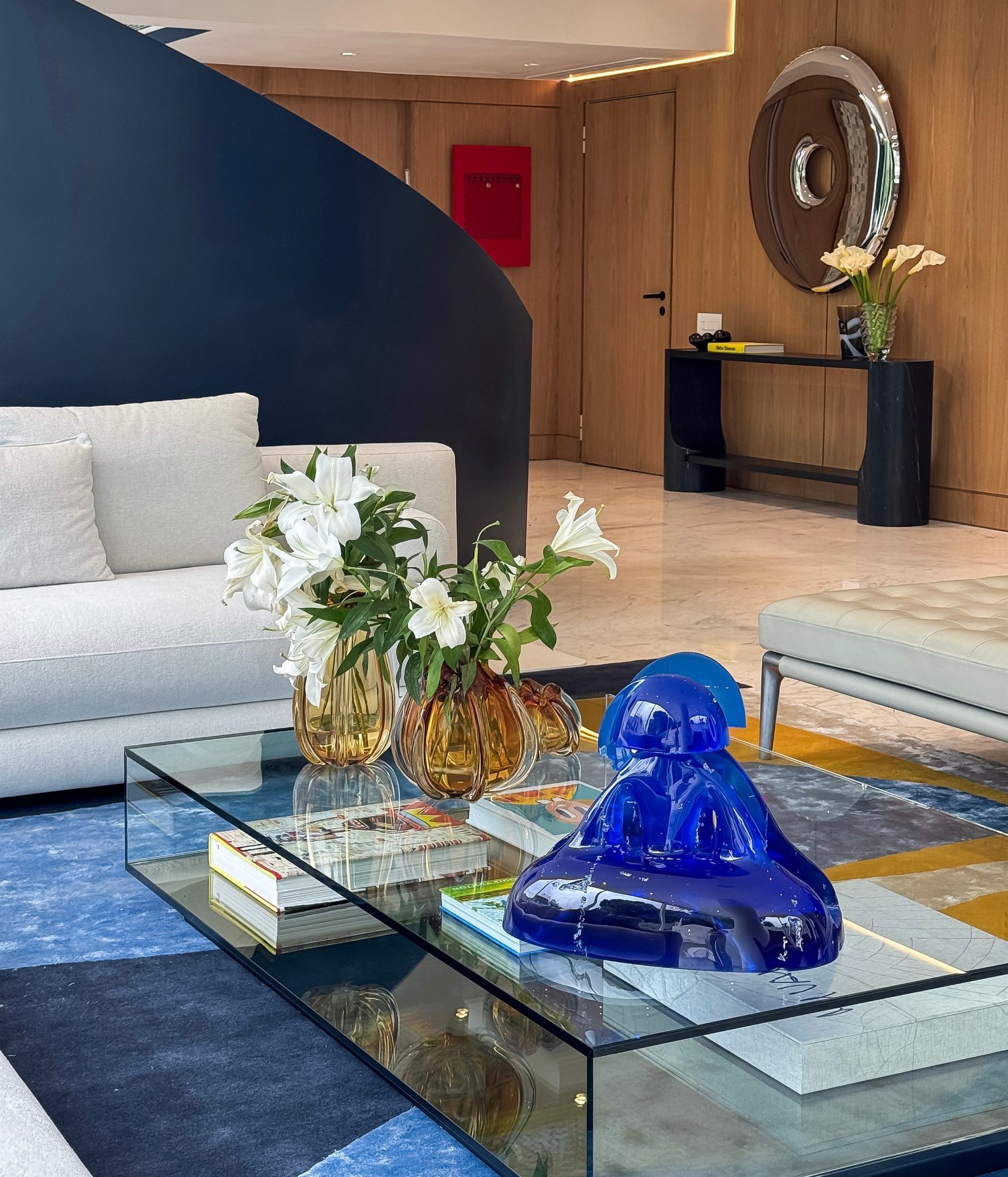 Spacious living room with white modular sofa, glass coffee table with art books and blue decorative sculpture