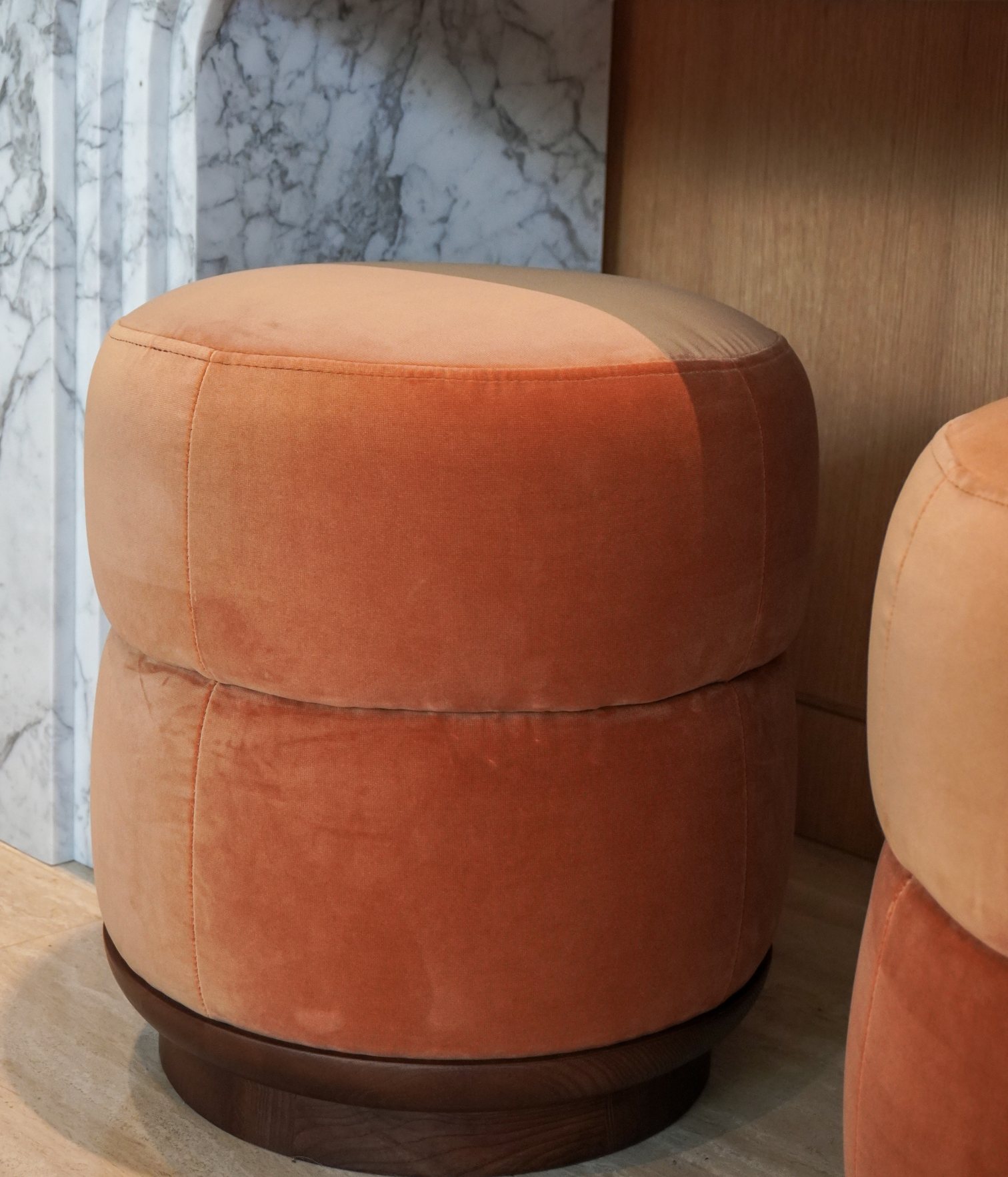 Puff tapizado en terciopelo terracota con base de madera junto a pared de mármol y paneles de madera