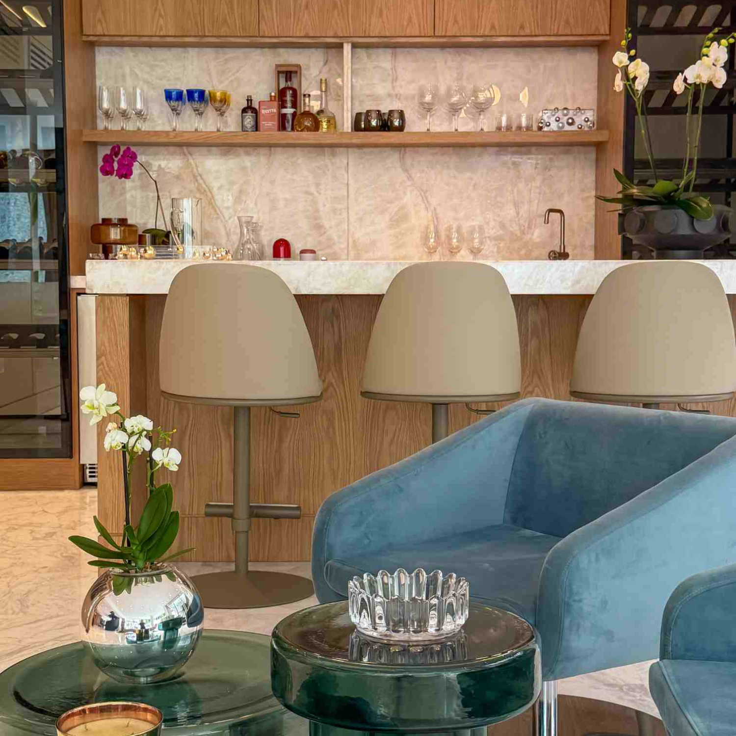 Salón residencial contemporáneo con sillones blancos, mesa de centro con plantas y consola decorativa con flores sobre pared de madera.