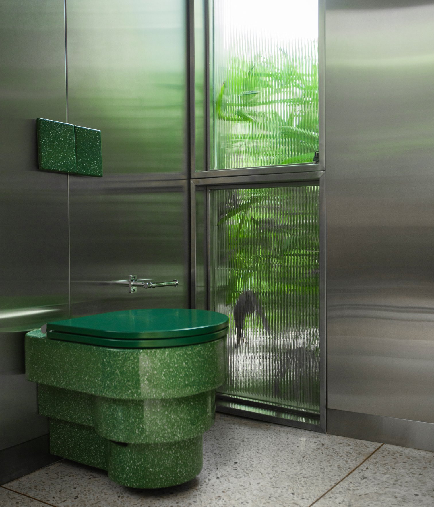 Baño con revestimiento metálico, inodoro verde y ventana con vidrio texturizado