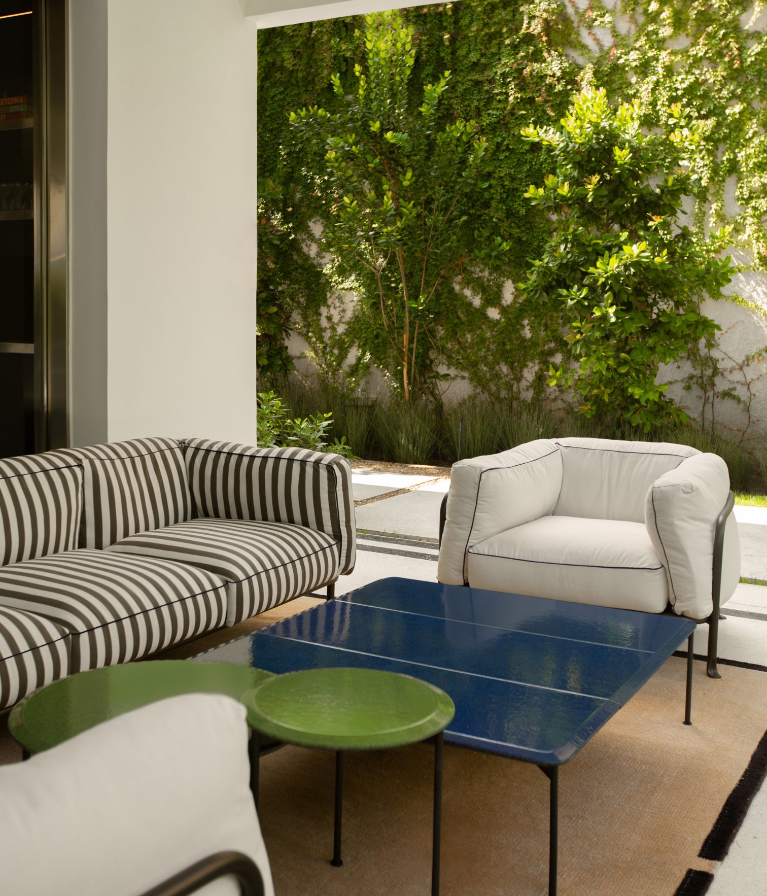 Terraza contemporánea con sofá rayado, sillones tapizados y mesas de centro frente a jardín vertical