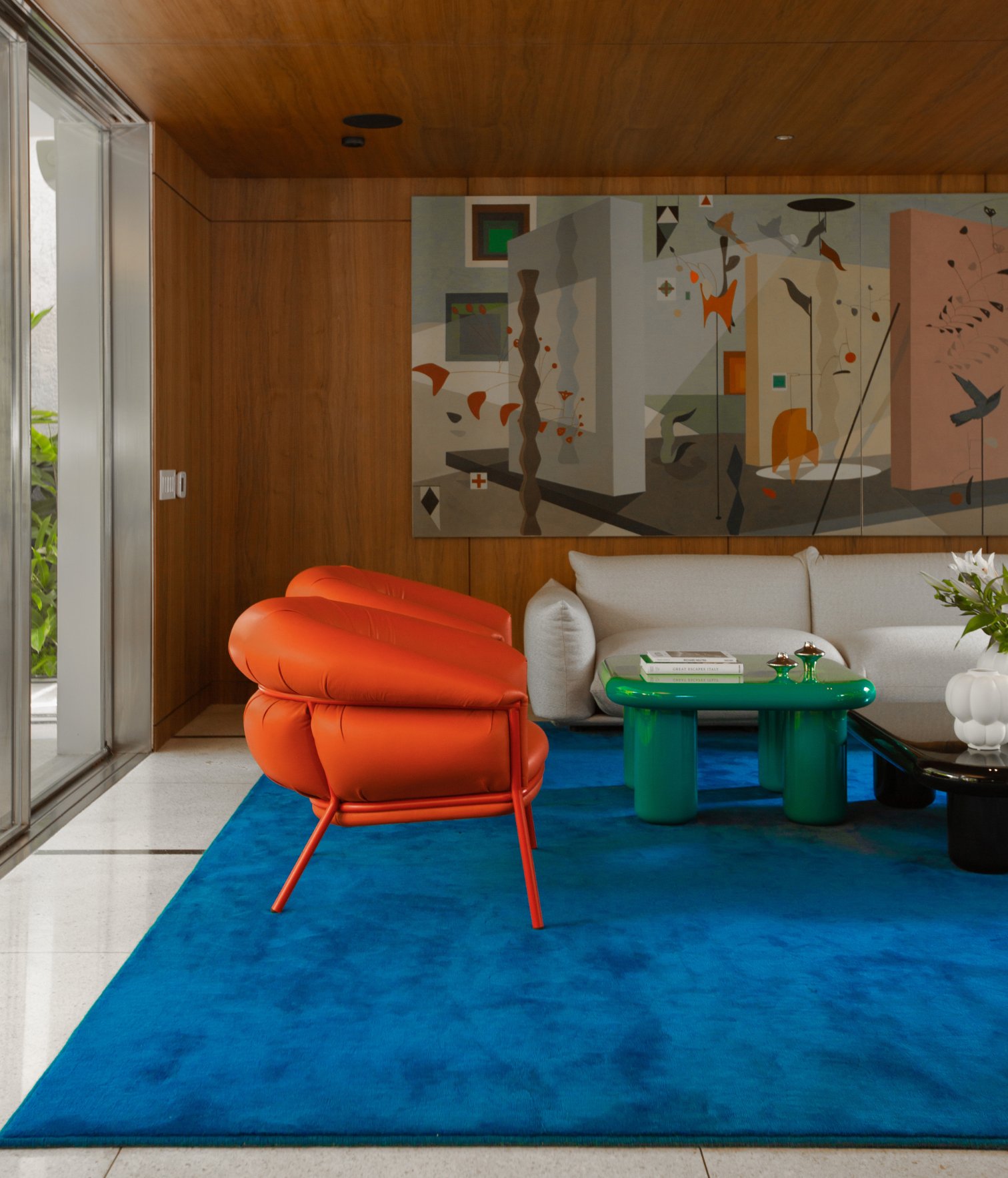Living room with a neutral-colored sofa, an orange armchair, a blue rug, and abstract art