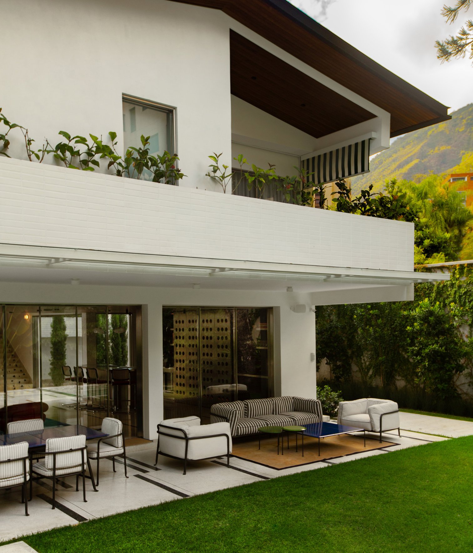 Fachada de residencia moderna con terraza cubierta, mobiliario exterior y jardín