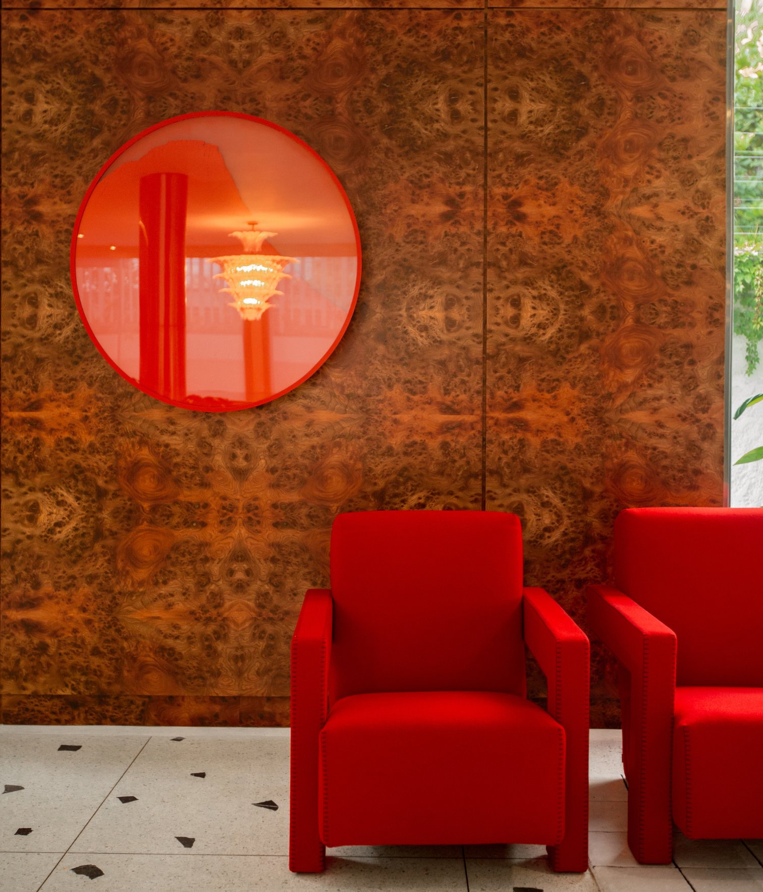 Sillones rojos frente a pared de madera con espejo circular decorativo